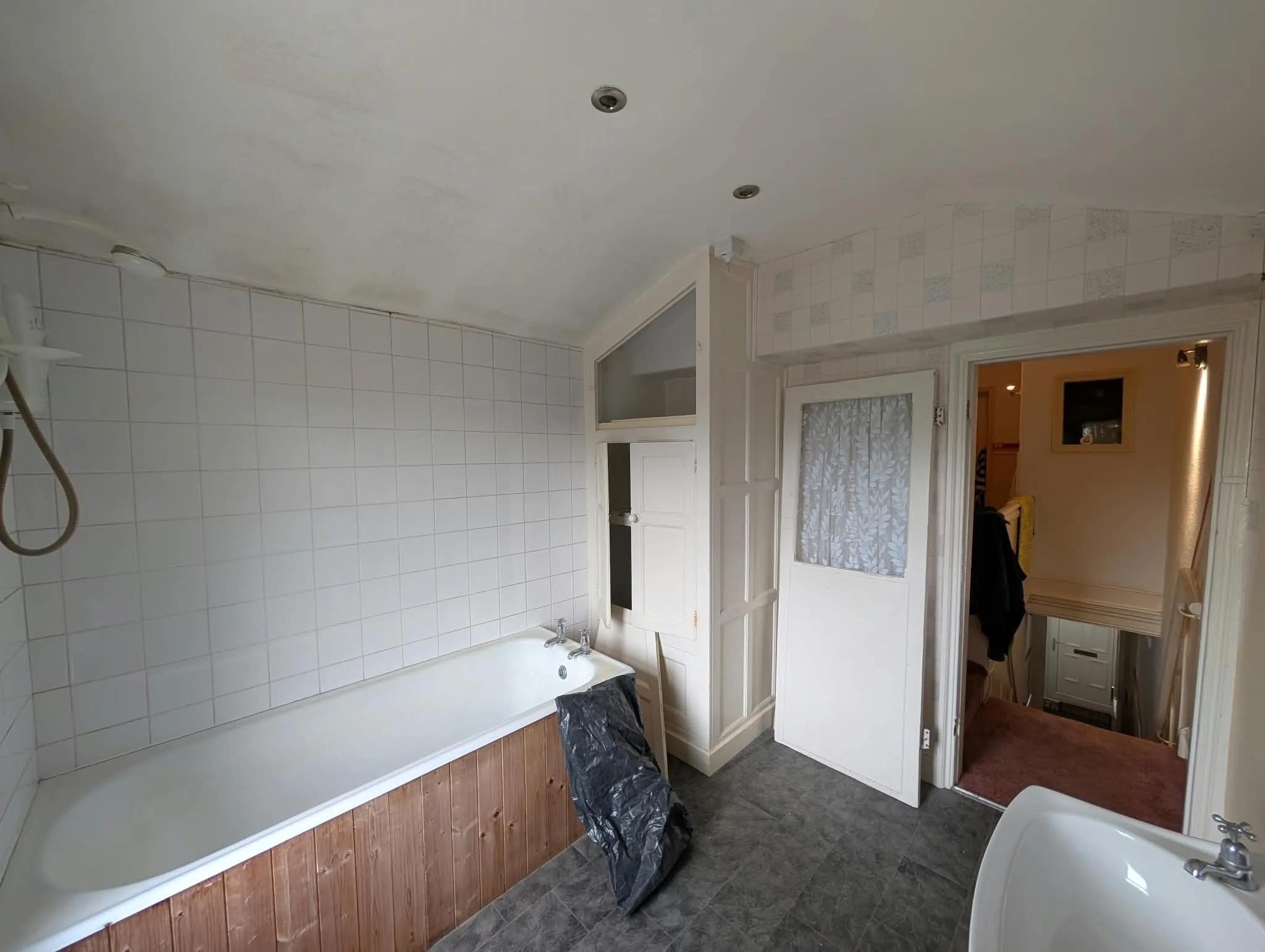 Existing bathroom with a timber bath panel and white square tiles.