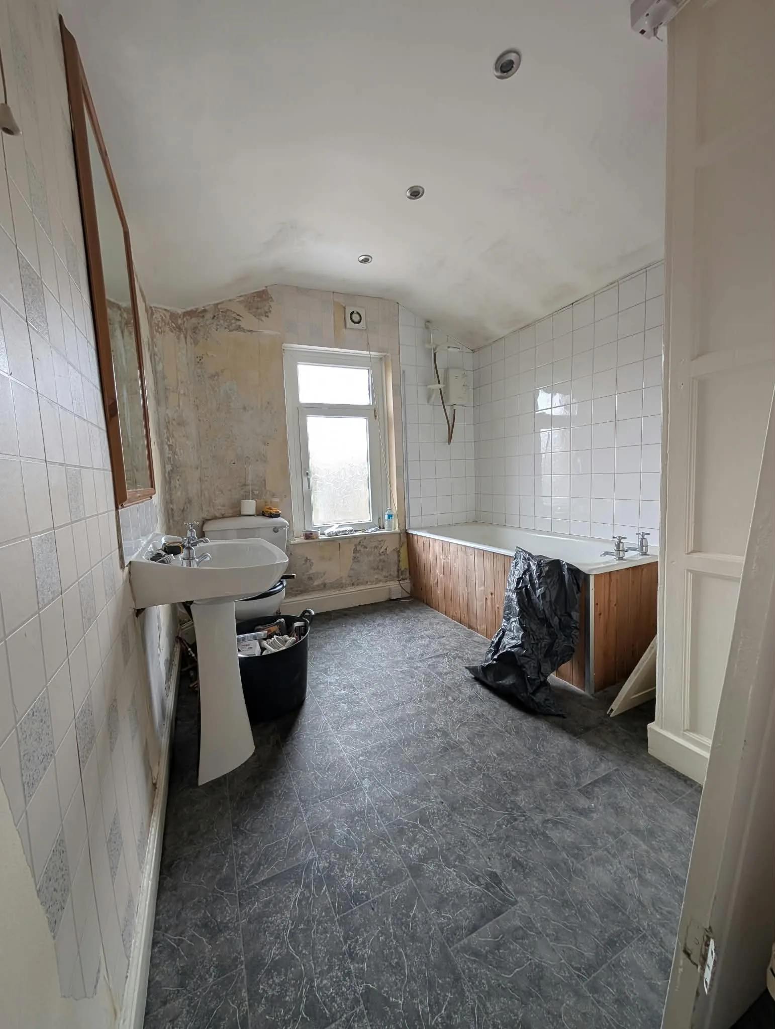 Portrait view of the original bathroom with a timber-panelled bath and pedestal basin.