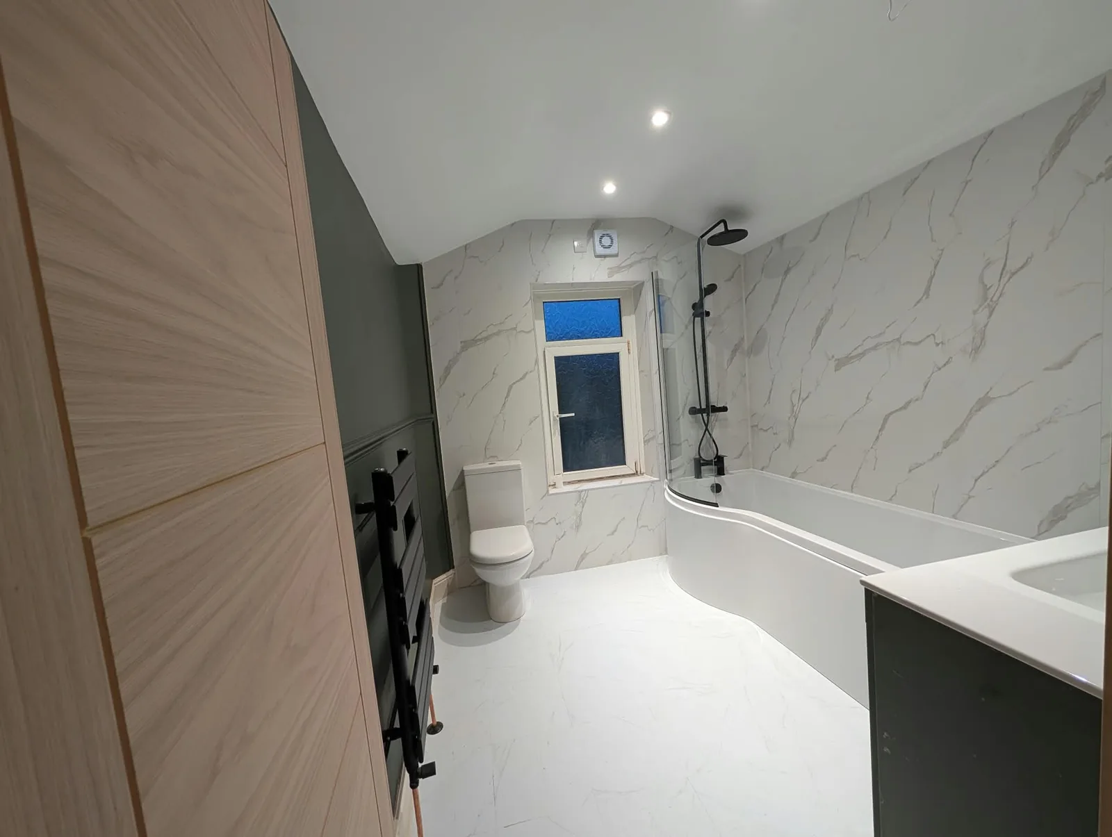 Renovated bathroom with green panelling, black fittings and marble-effect surfaces.