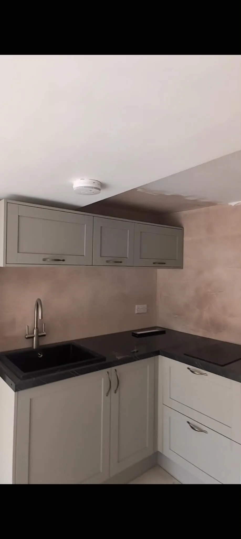 Grey kitchen cabinets and a sink fitted against unpainted plaster.