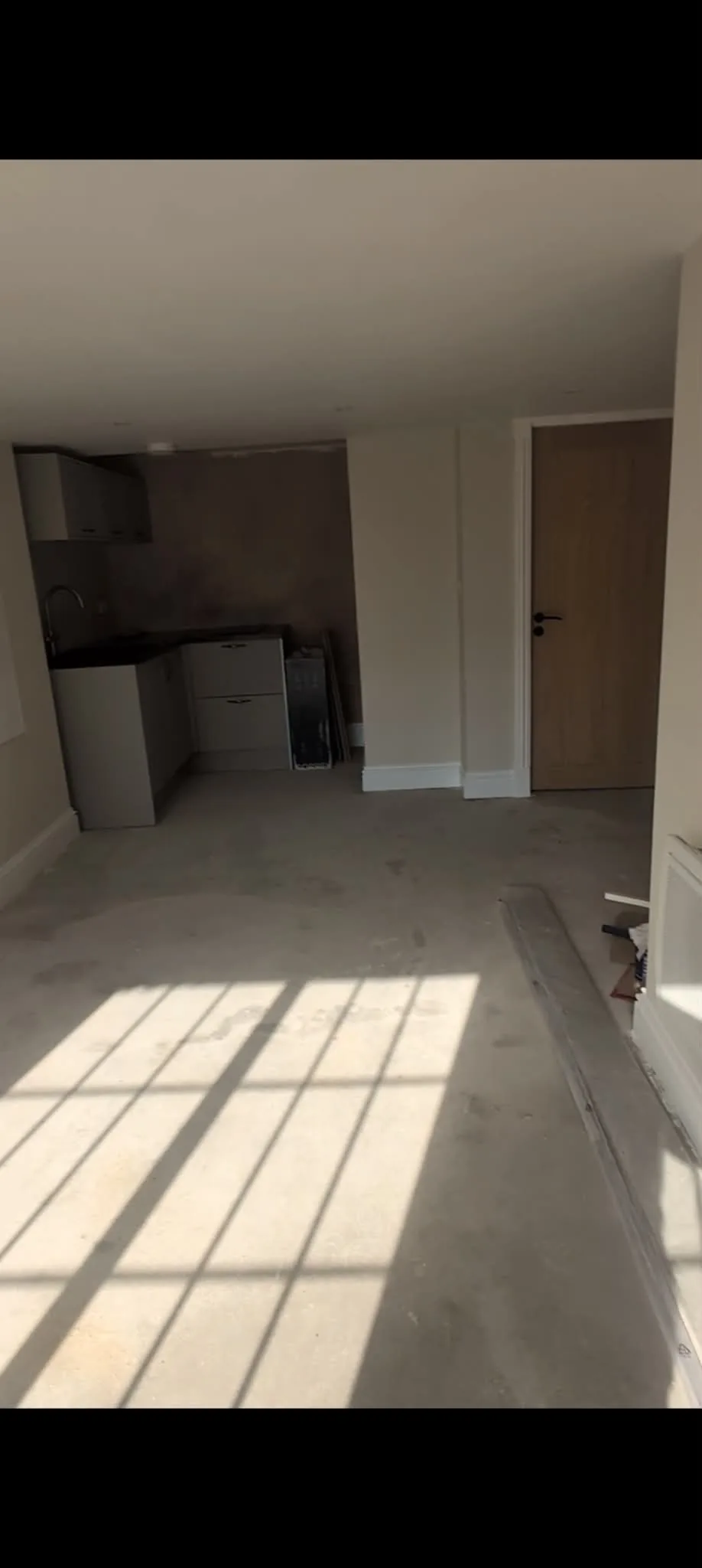 Compact kitchen fitting within a newly plastered room with an unfinished floor.