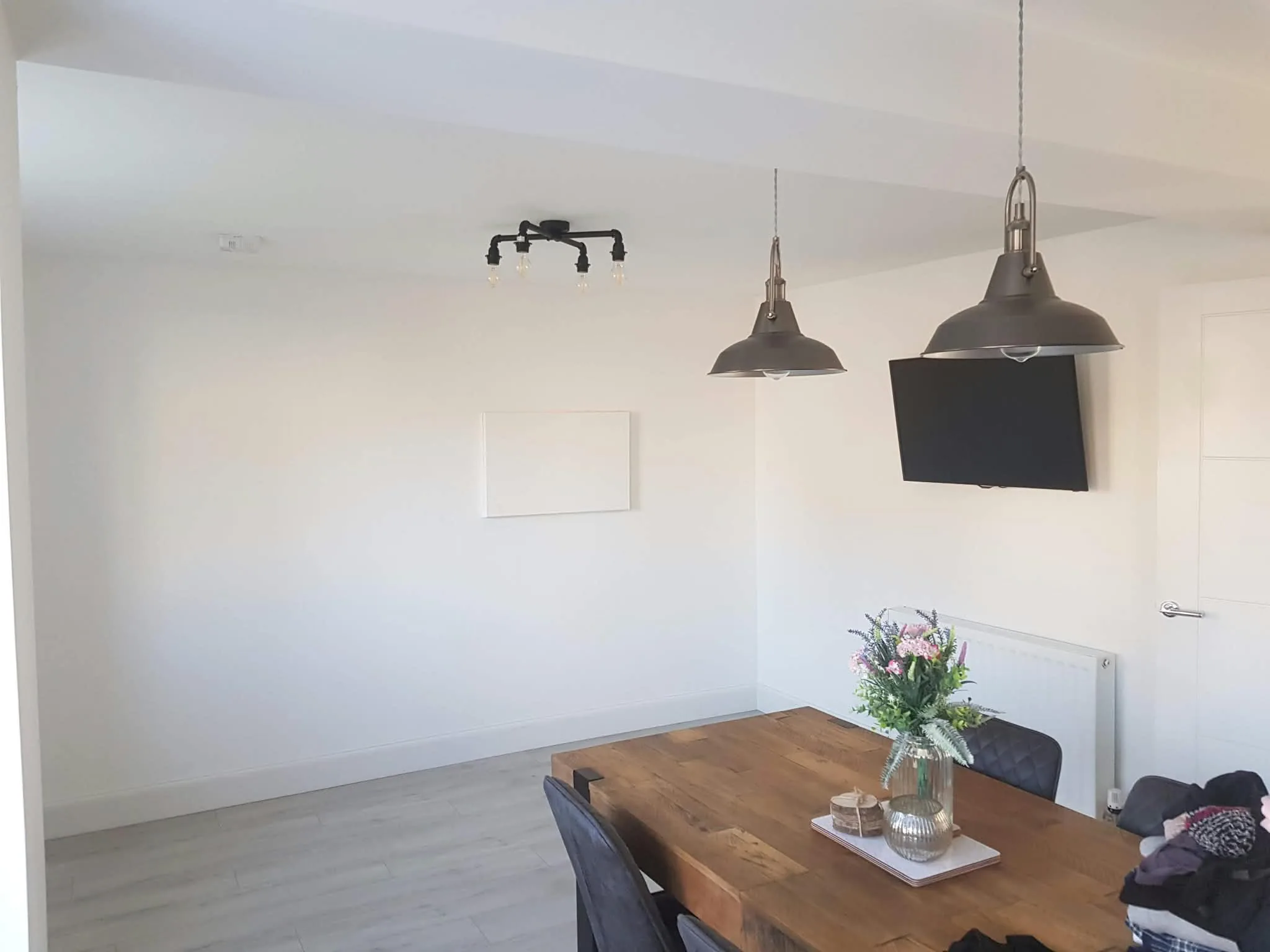 Bright dining room with a timber table, flowers and grey pendant lights