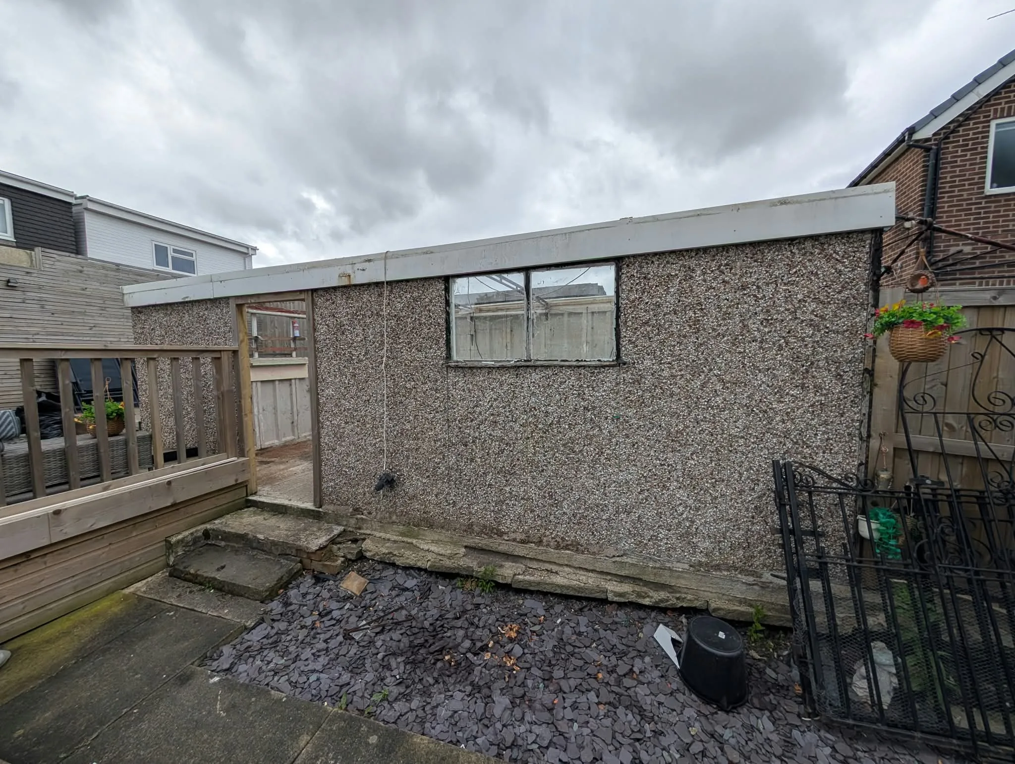 Old pebbledash garage side with timber door and window beside decking.