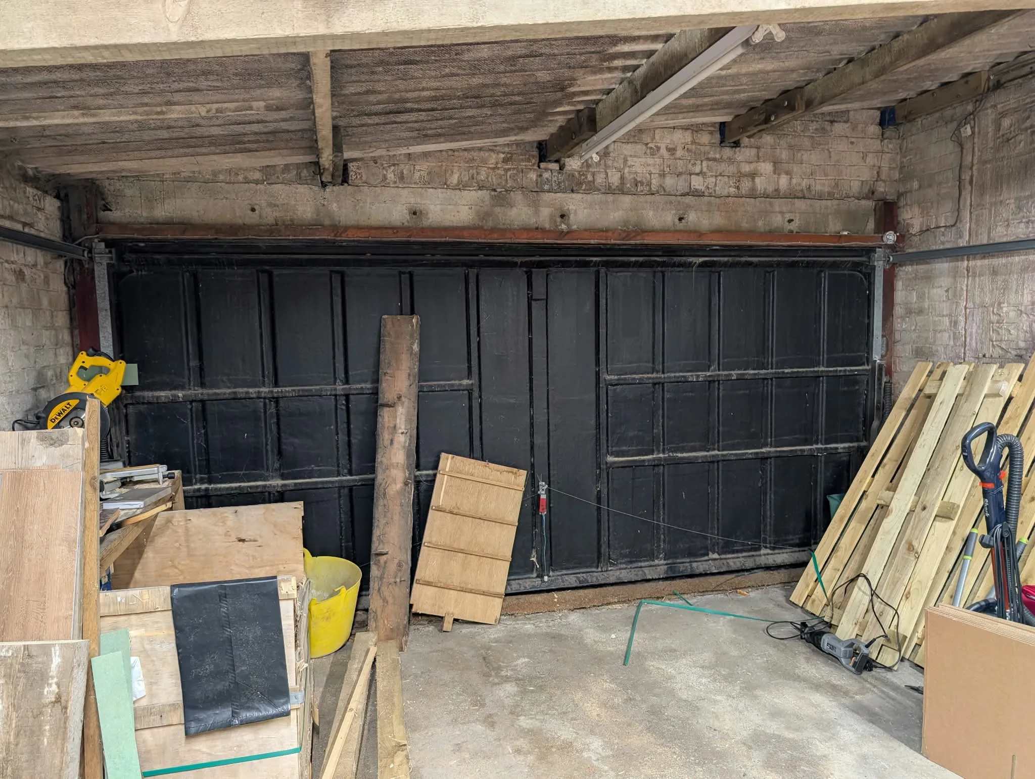Existing black garage doors viewed from inside, with timber and tools.