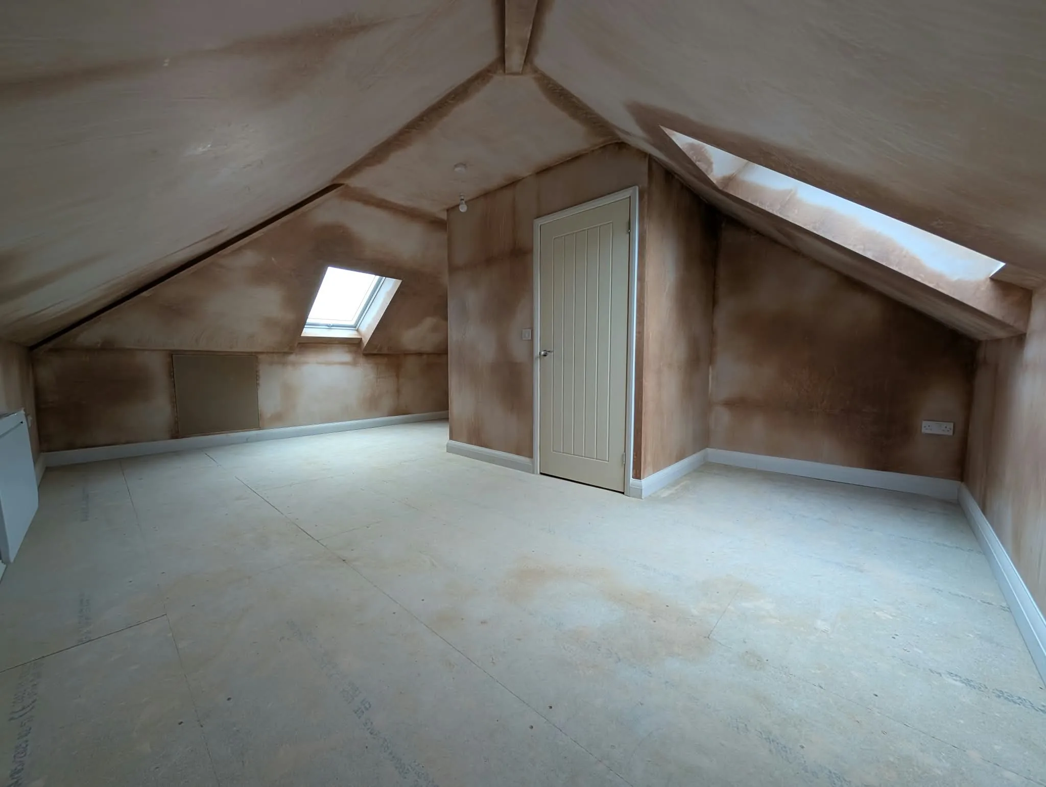 Freshly plastered loft room with rooflights and an unfinished floor.