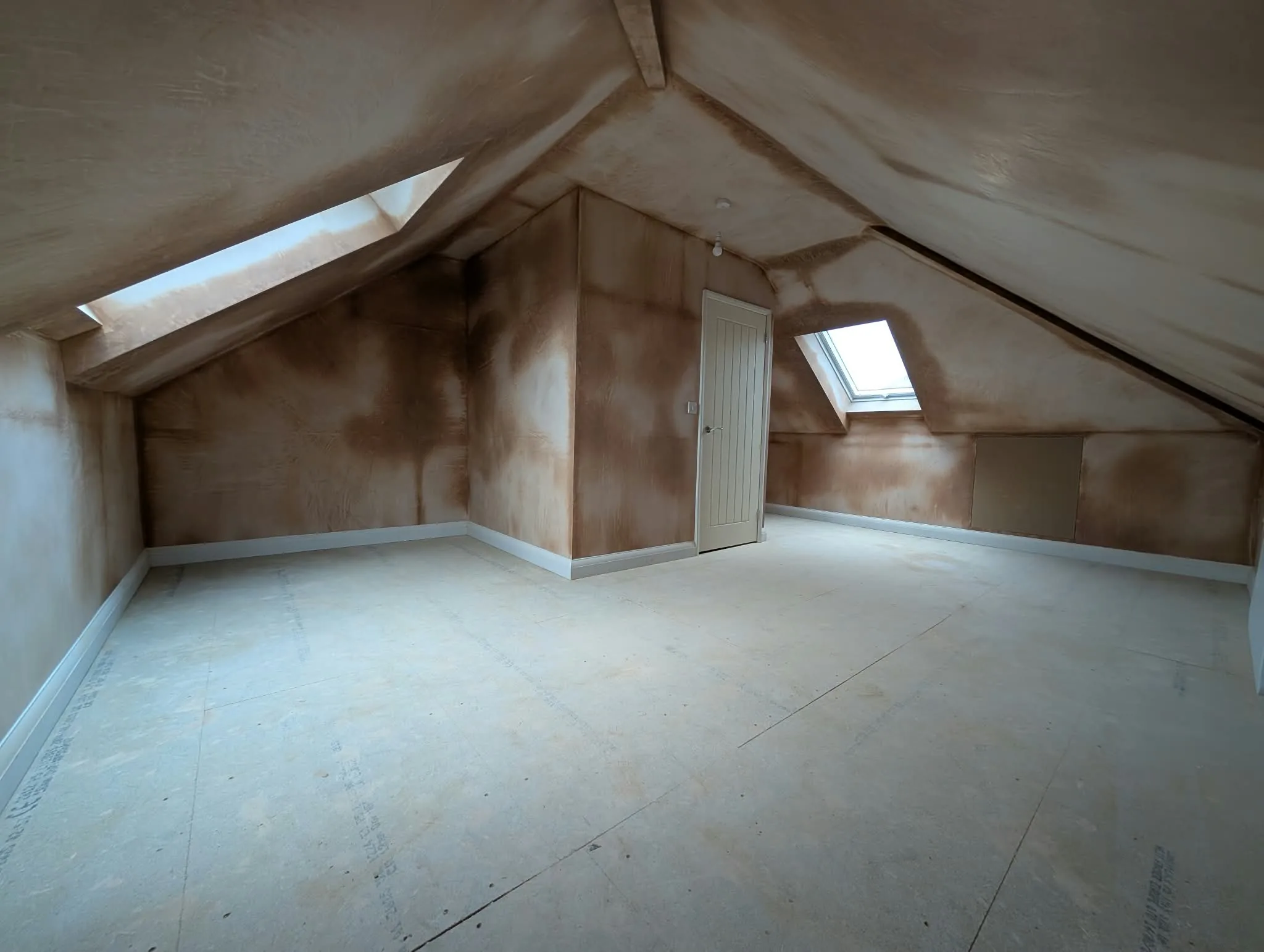 Plastered loft room with two rooflights, a fitted door and unfinished floor.