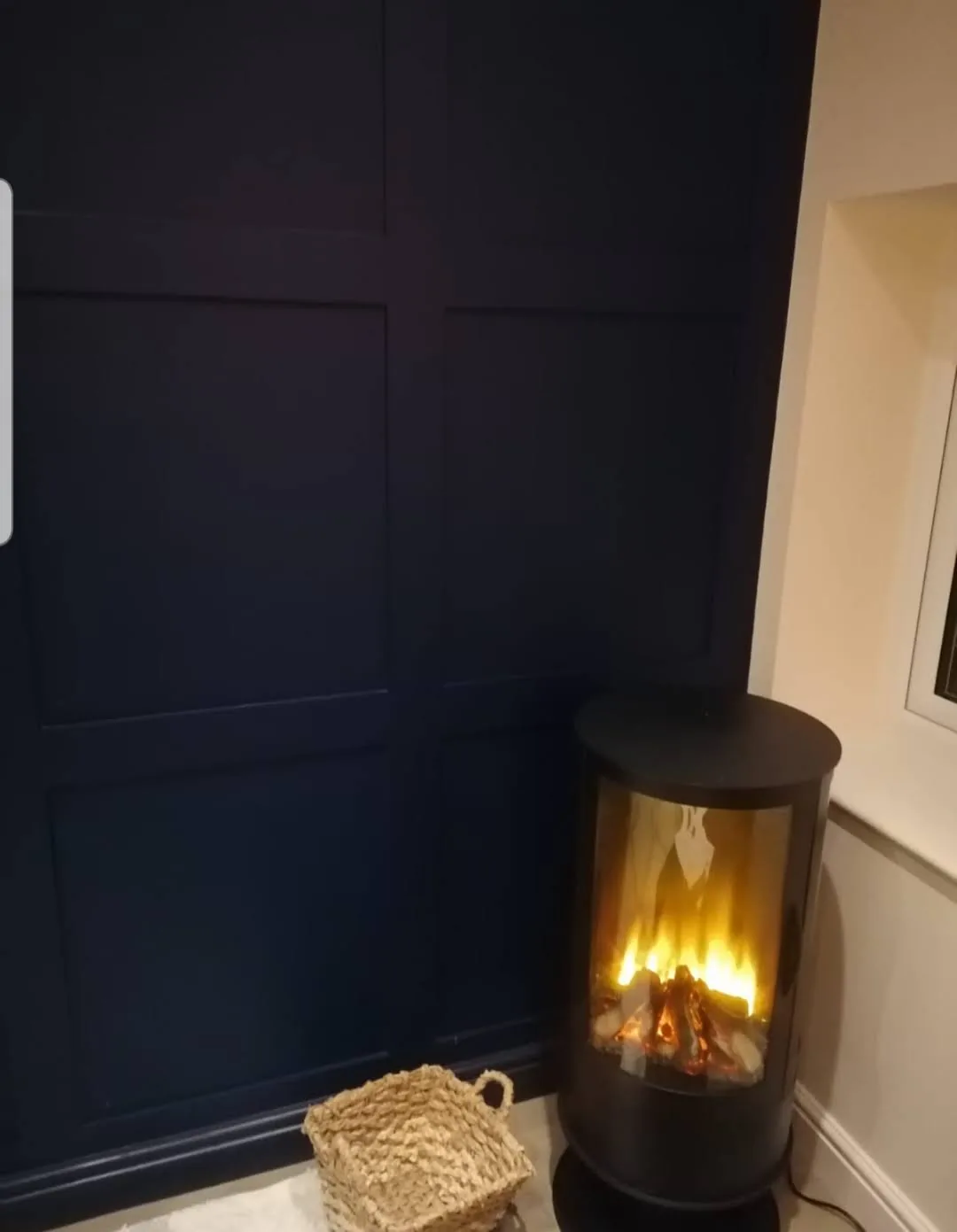 Navy wall panelling behind a black electric stove and wicker basket.