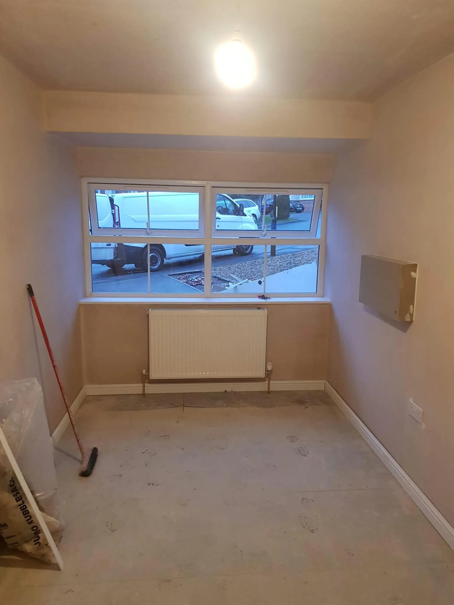Newly plastered room with a white window, radiator and unfinished floor.