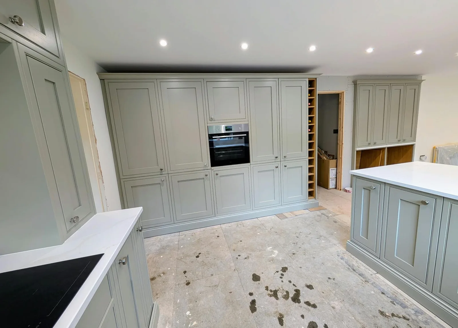 Pale shaker kitchen cabinets and white worktops during installation, before the floor is finished.